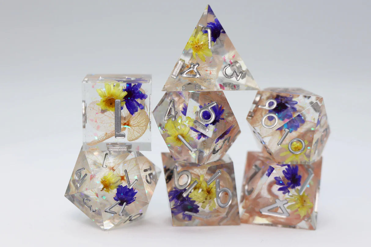 Sharp Edge Resin RPG Dice Set - Wildflower Meadow, 7 clear dice with yellow and blue flowers inside.