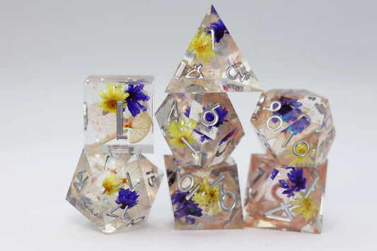 Sharp Edge Resin RPG Dice Set - Wildflower Meadow, 7 clear dice with yellow and blue flowers inside.