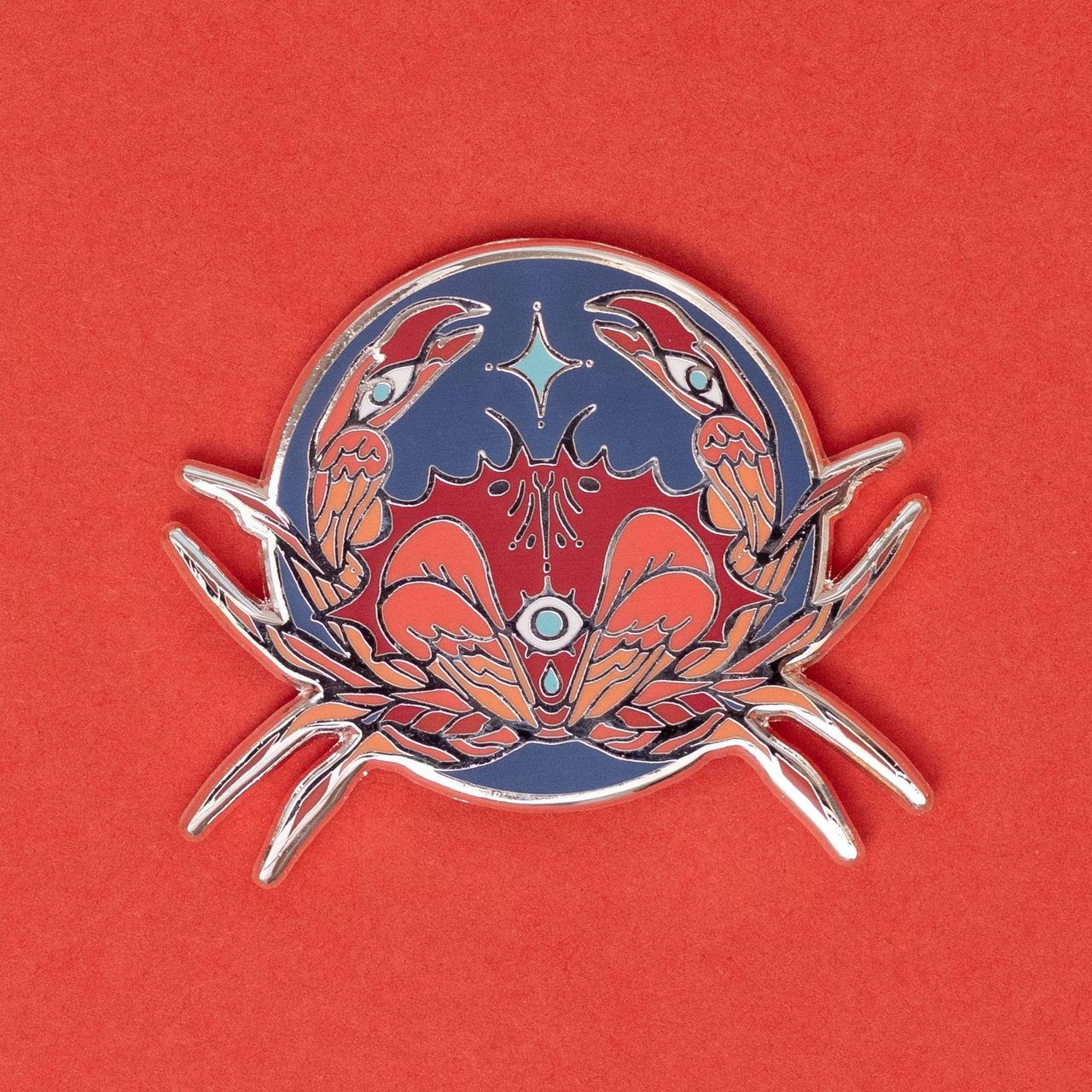 Angelic Crab Pin, silver-plated enamel, features two crabs with blue and red accents on a red background.