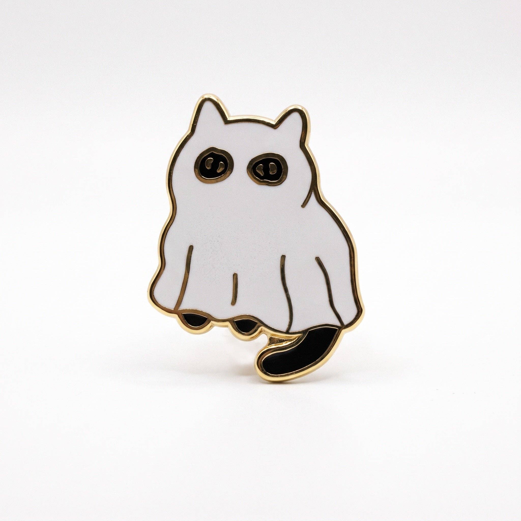 Gold-plated hard enamel pin of a cat wearing a white ghost sheet with black eyes and a tail.