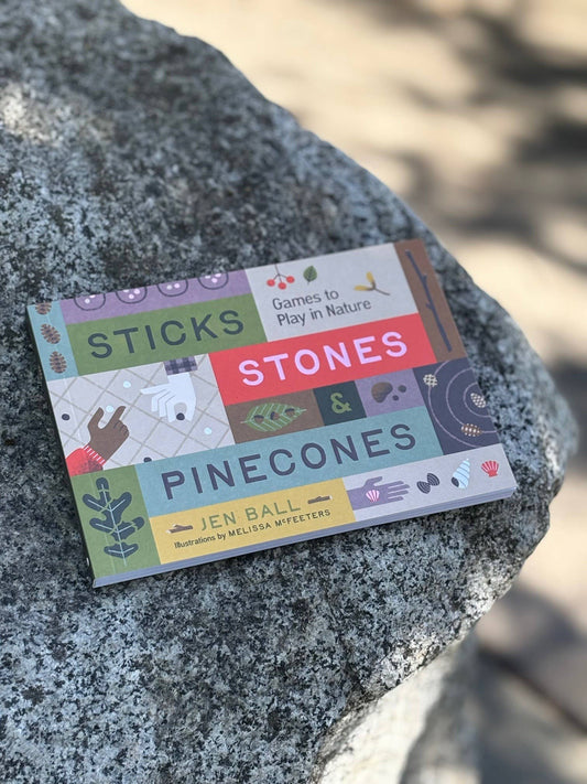 Sticks, Stones & Pinecones book displayed on a large rock outdoors in sunlight.