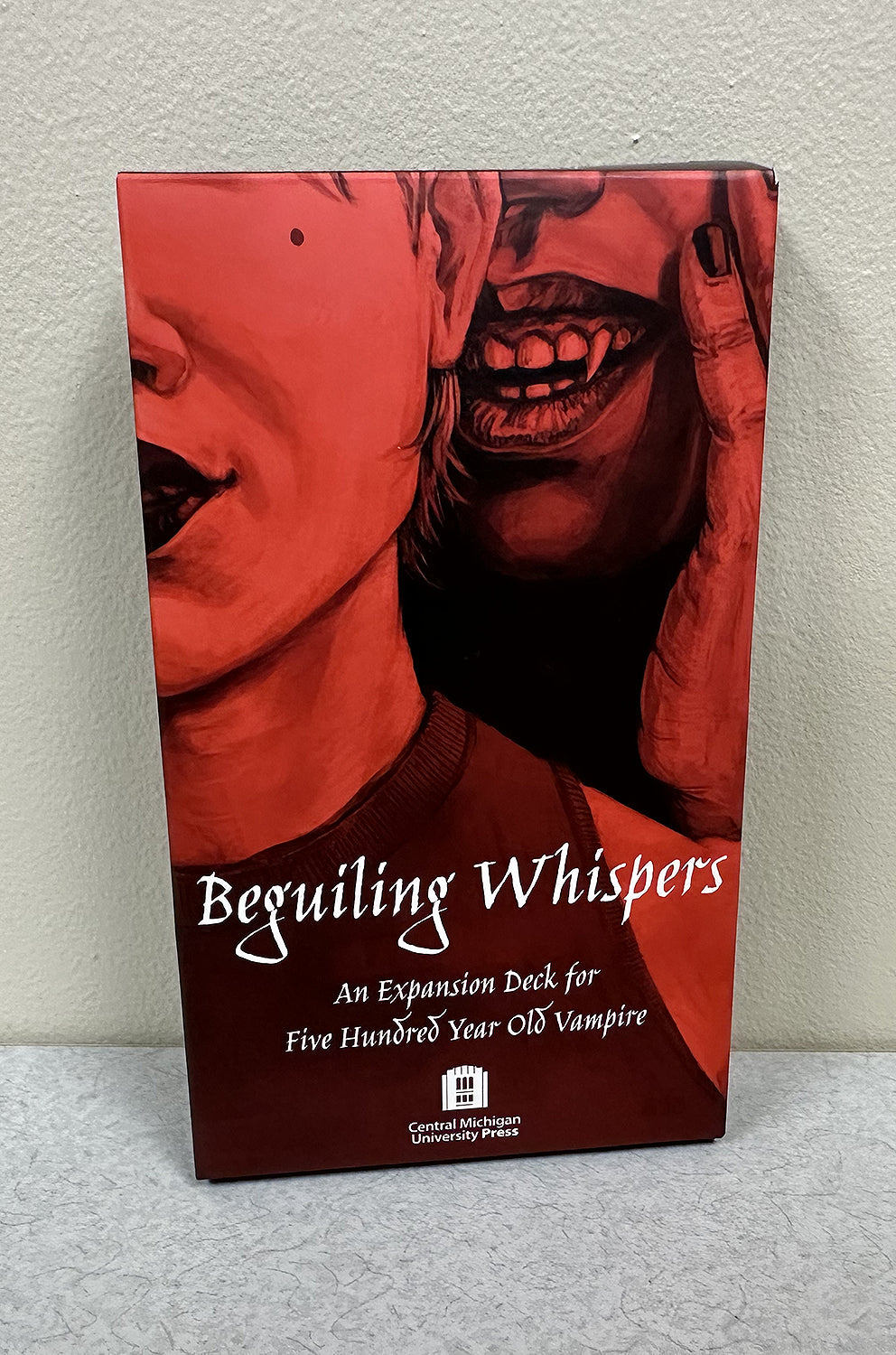 Beguiling Whispers game box, red-toned, showing two faces including one with vampire fangs, variant: Five Hundred Year Old Vampire.