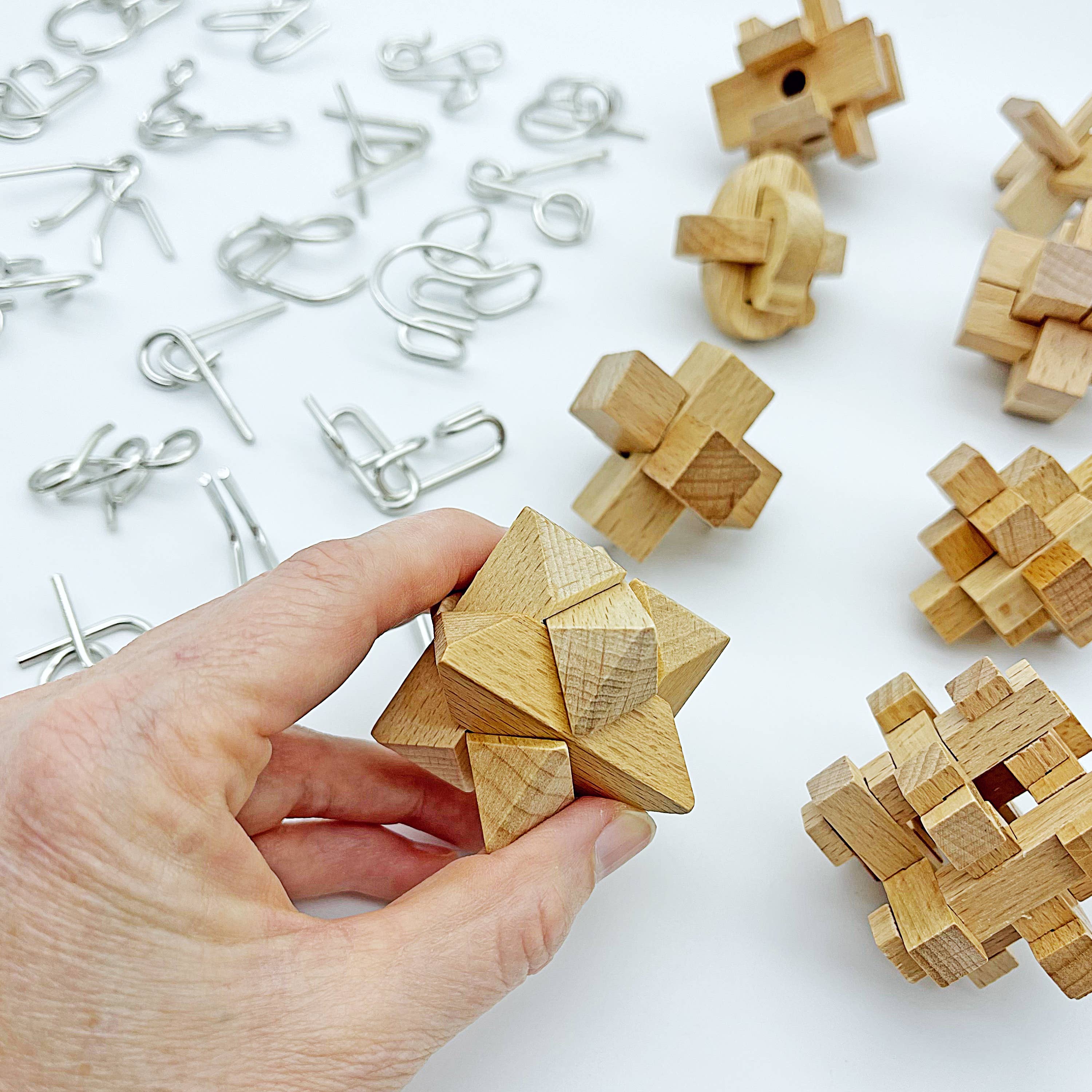 Hand holding True Genius Museum Collection 30-piece set with wood and metal brainteasers scattered.