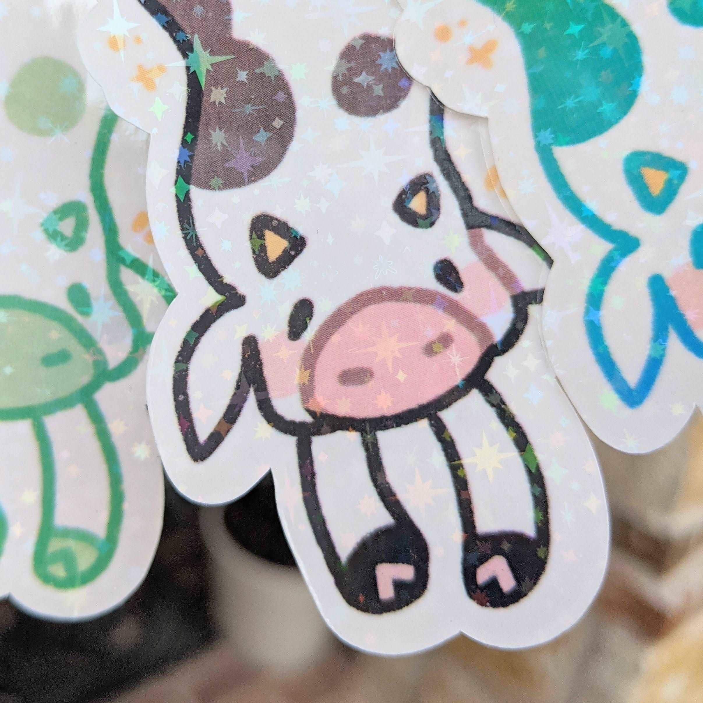 Sparkly long cow stickers with a glittery cow, pink snout, brown spots, stars. Waterproof design.