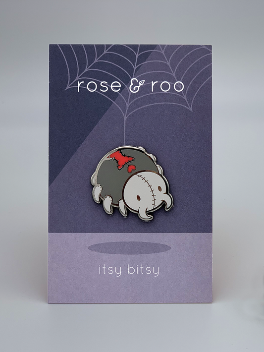 The Itsy Bitsy Enamel Pin shows a stitched zombie black widow spider on a backing card with text and web details.
