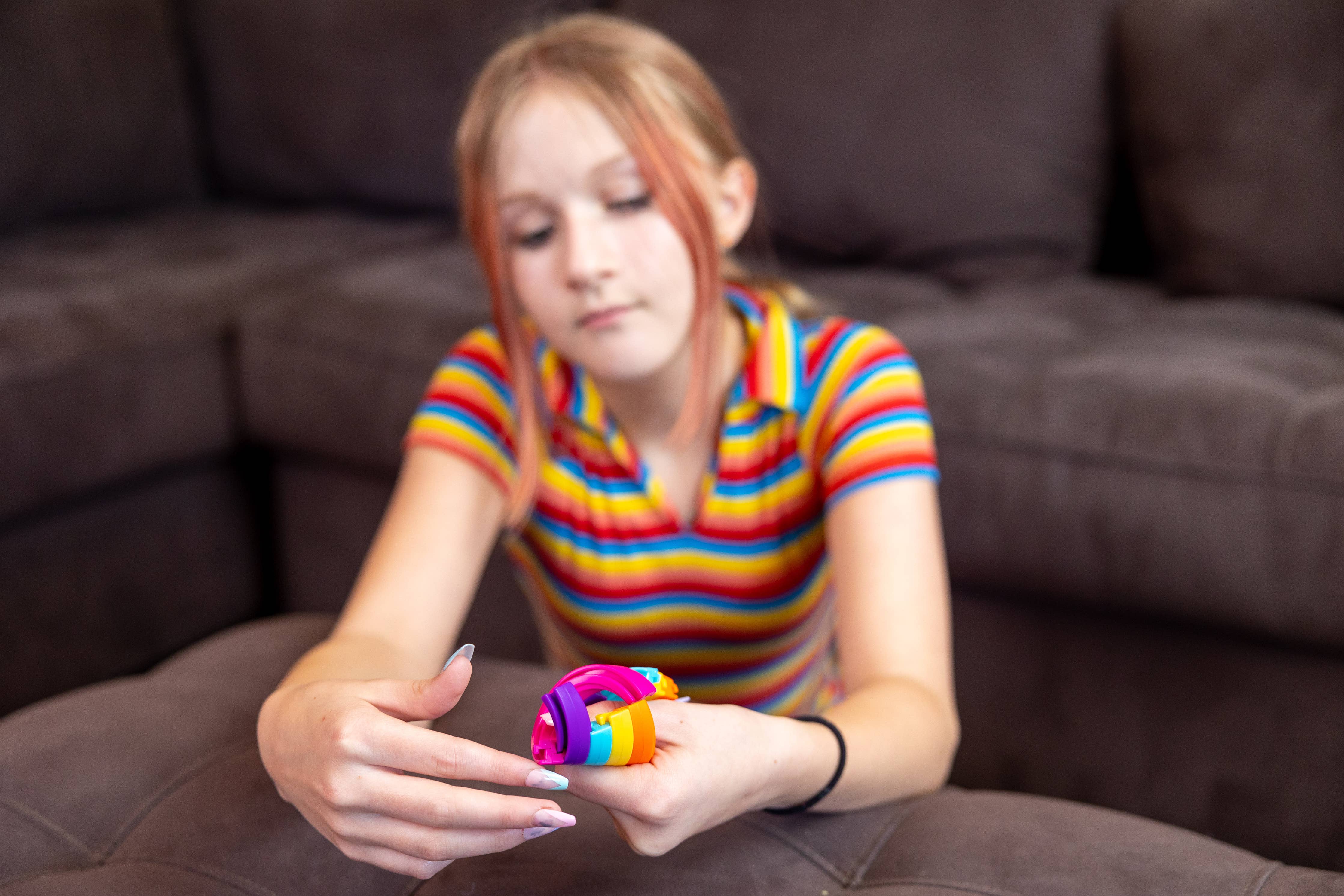 Hypno-Twist Rainbow Fidget held by a girl wearing a rainbow-striped shirt, seated on a couch.