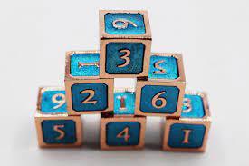 Blue and Copper D6 Metal Dice Set stacked in a pyramid next to a leather spell book.