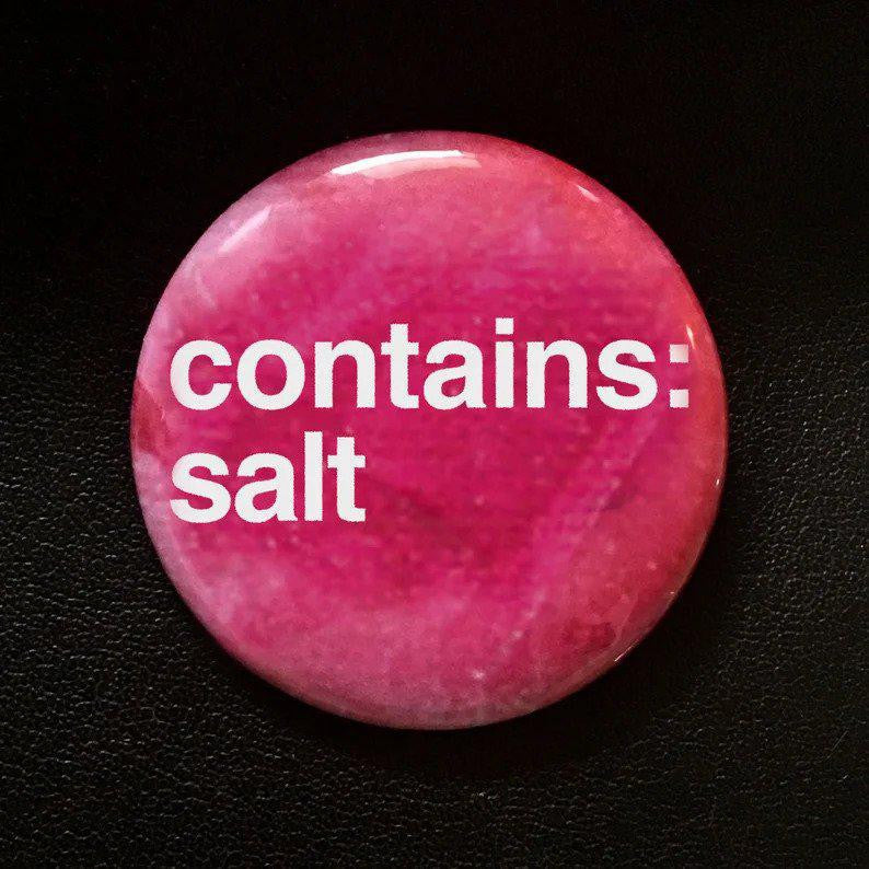 Round, pink 1.25 button pin with white contains: salt text on a black background.