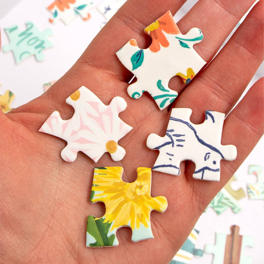 Hand holding Tea Time 500 Piece Jigsaw Puzzle featuring floral pieces and animal art.