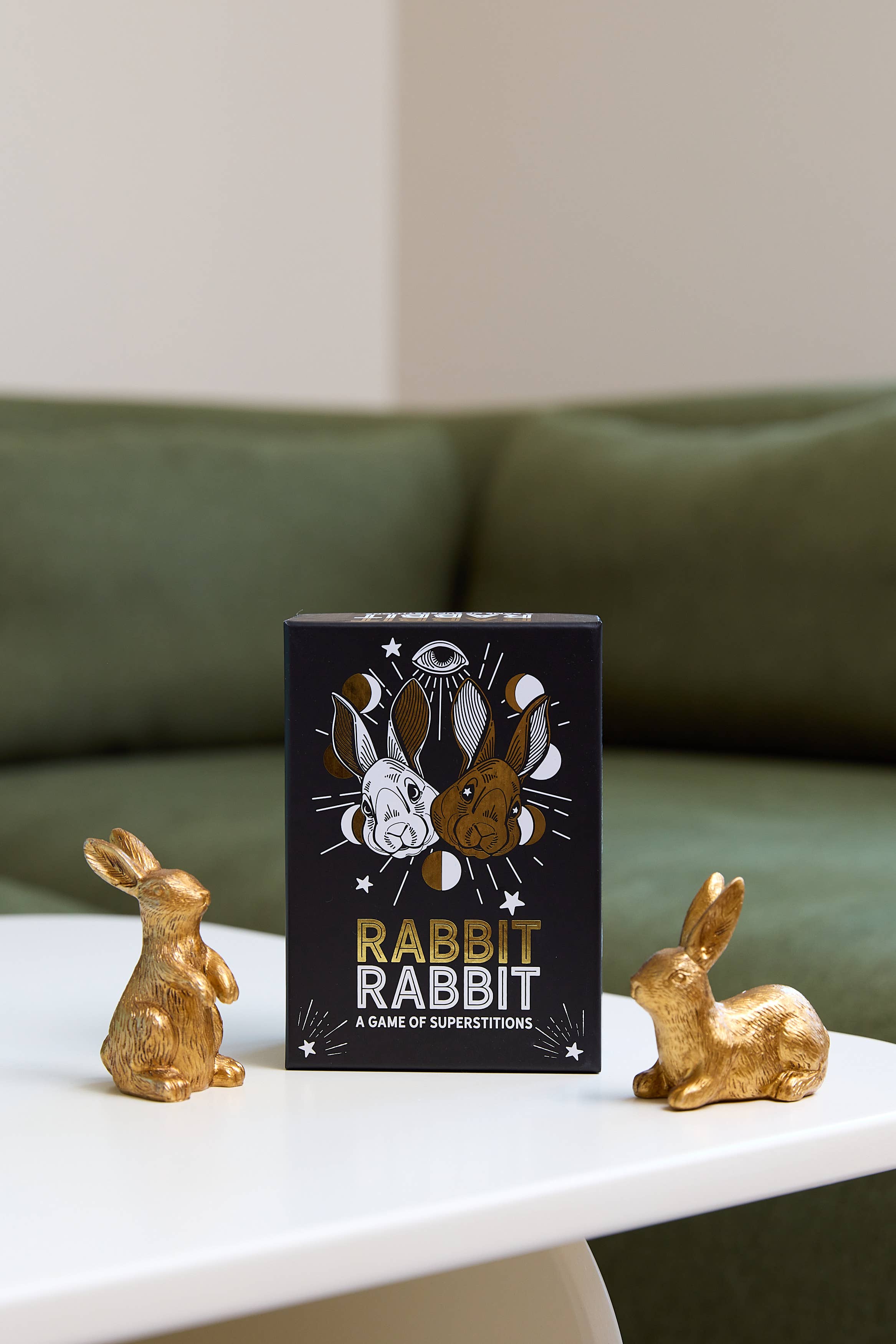 Rabbit Rabbit: A Game of Superstitions black box on a table between two gold rabbit figurines.