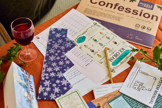 The Confession Escape Room Puzzle Board Game with puzzles, pen, drink, and holly leaves on a tabletop.