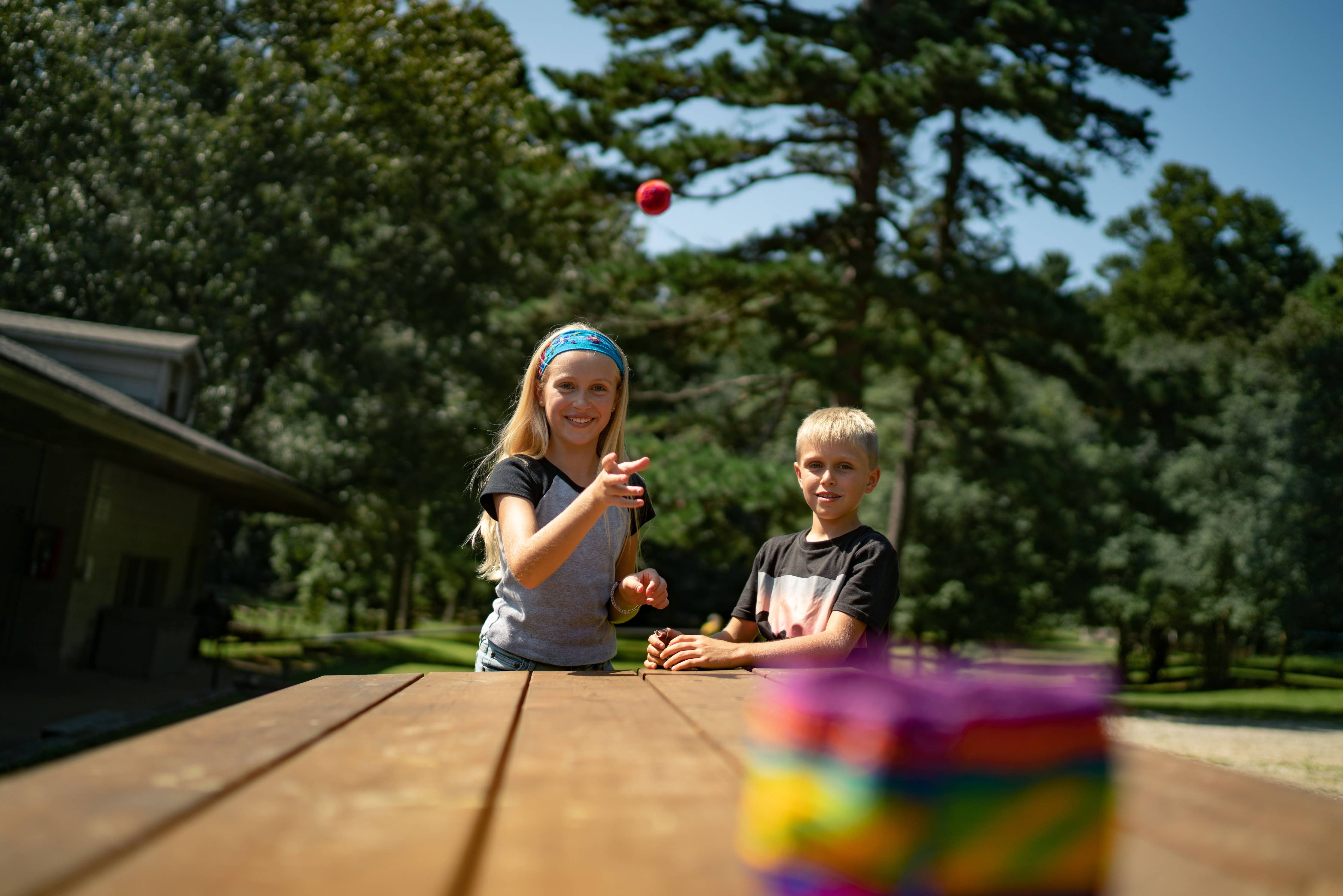 Two children play Canastaball with Hacky Sacks, tossing them at a colorful outdoor target.