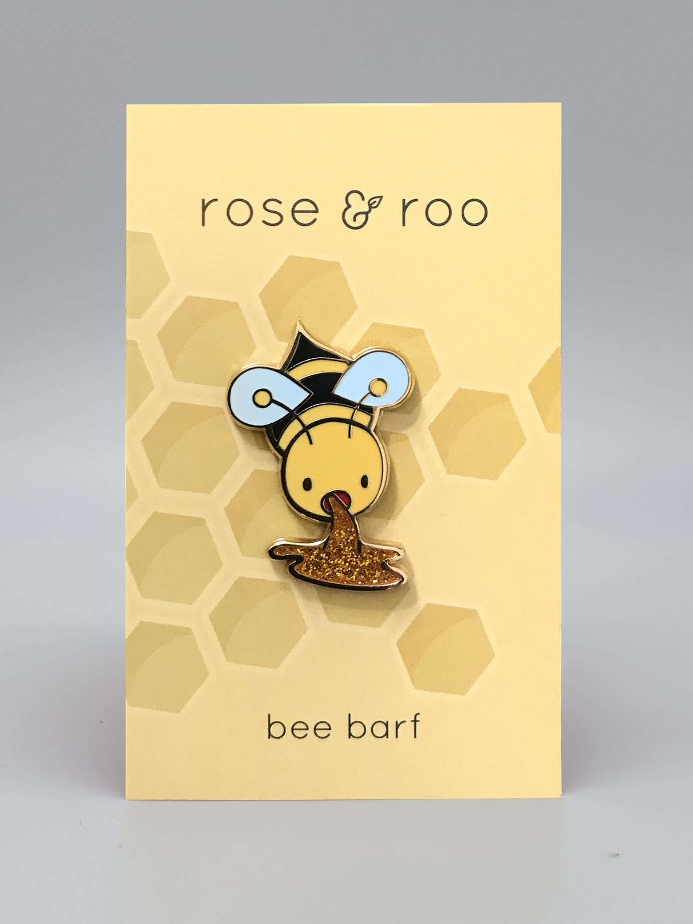 Bee Barf Enamel Pin featuring a gold bee appearing to vomit glitter honey.