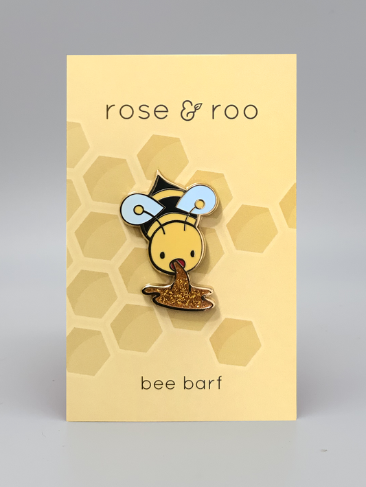 Bee Barf Enamel Pin featuring a gold bee appearing to vomit glitter honey.