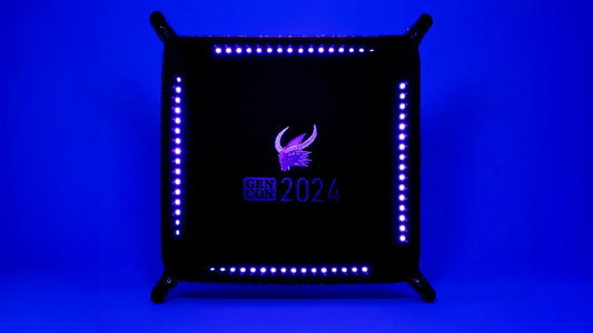 Gen Con 2024 UV Black Light Dice Tray, black and square with a winged logo and blue LED lights.