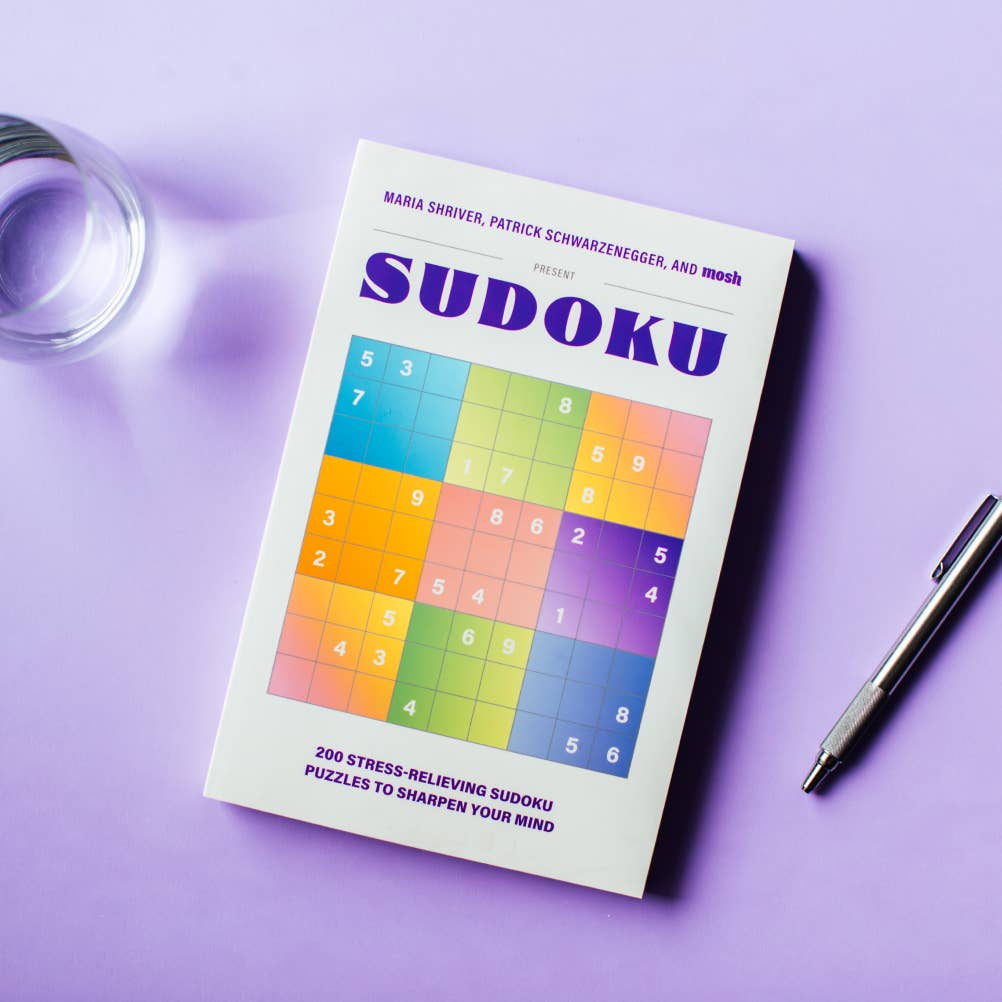 Sudoku book by Blue Star Press with pen and glass of water on a purple surface.