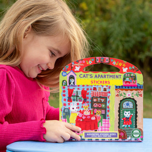 Cats Apartment Stickers set held by a young girl in a pink shirt at an outdoor table.