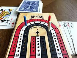 Cribbage Board 3 Track Color Coded with score pegs and playing cards on a wooden table.
