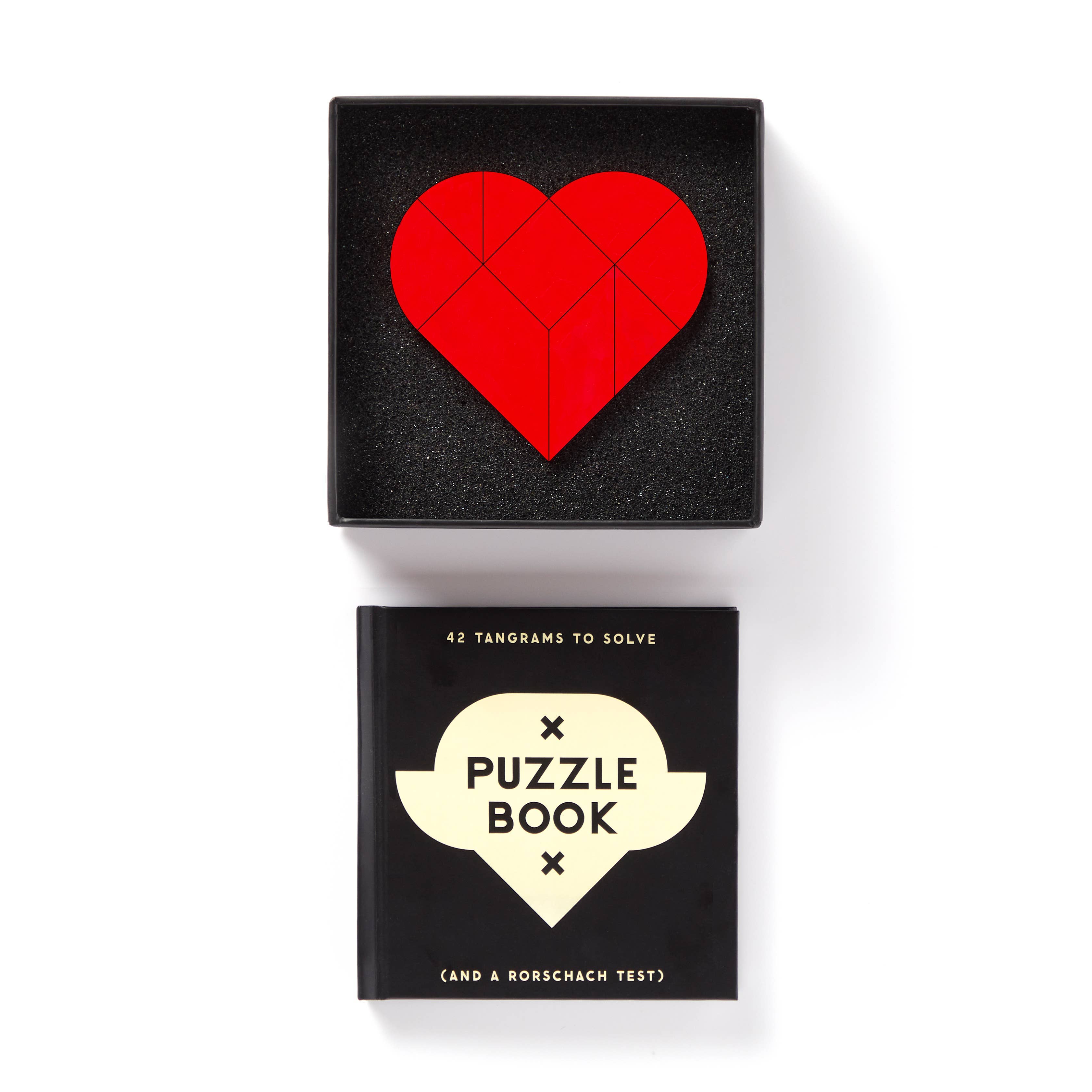 Brass Monkey At First Sight Tangram Puzzle with red heart design, placed above a black book.