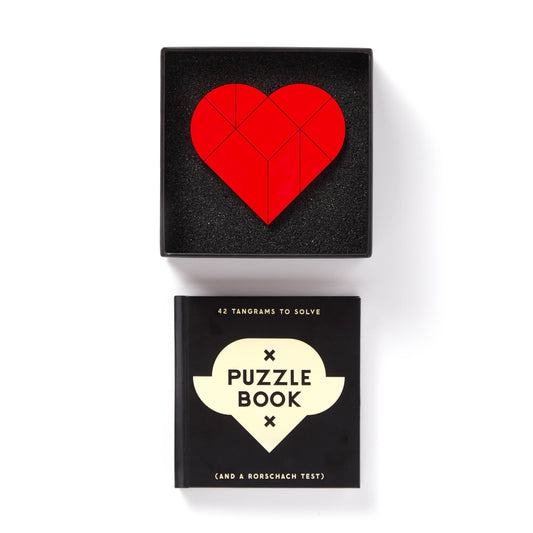 Brass Monkey At First Sight Tangram Puzzle with red heart design, placed above a black book.