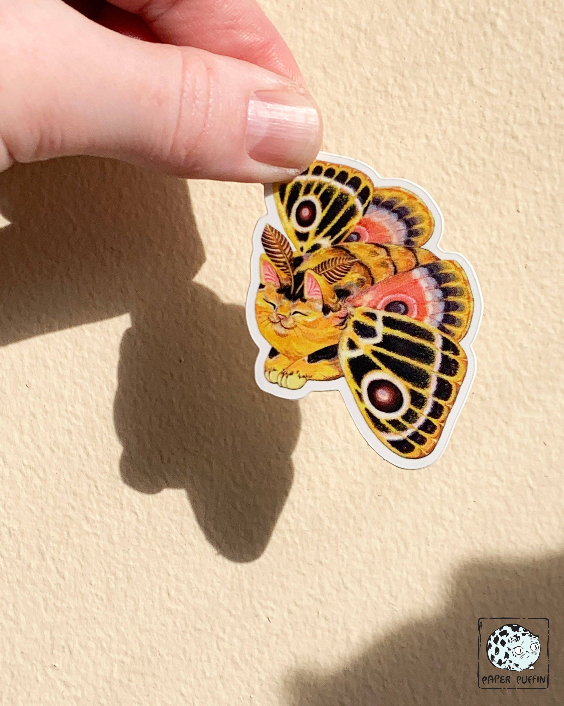 Moth Cat Vivid Joy sticker: a cat with yellow, orange, and black moth wings featuring eyespot patterns.