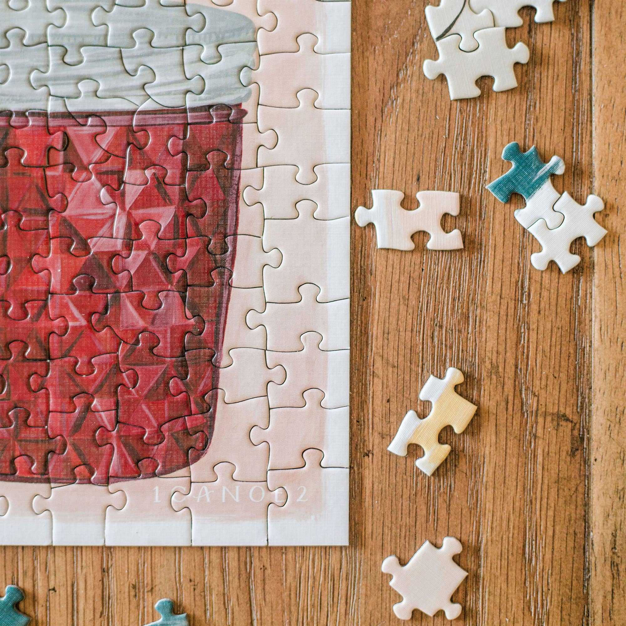 Simple Joys Puzzle, 1,000 pieces, hand-painted illustrations, some loose pieces on wooden surface.