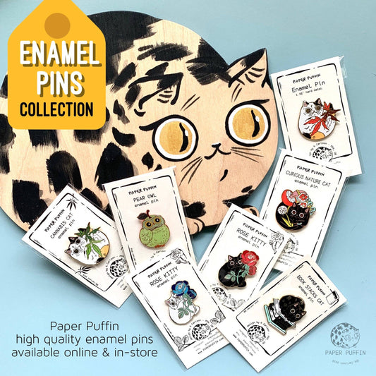 Six enamel pins, including a Book Stacks Cat Enamel Pin.