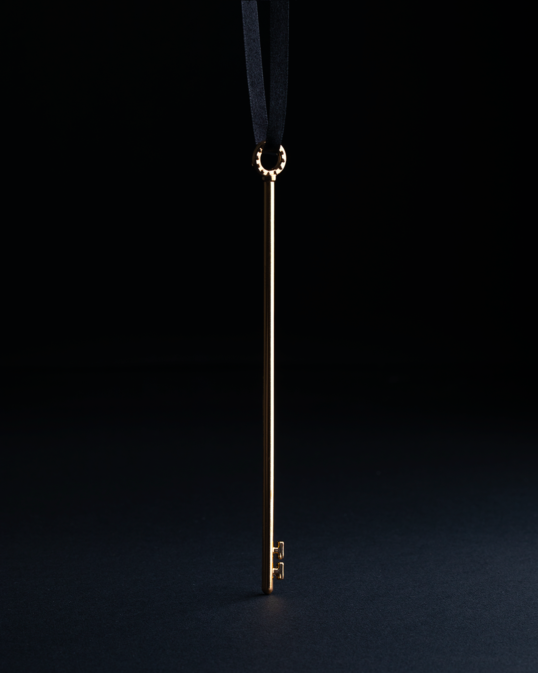 Skeleton Key Puzzle, a long, slender brass key on a black ribbon.