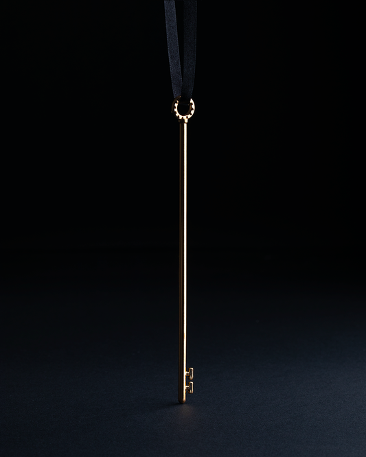 Skeleton Key Puzzle, a long, slender brass key on a black ribbon.