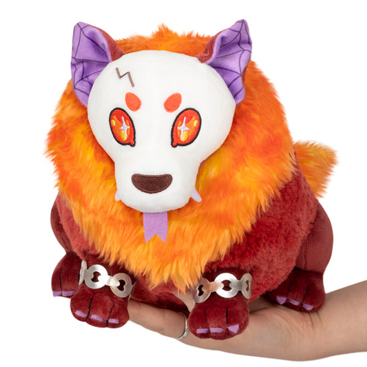 Mini Squishable Hellhound orange plush with skull mask, purple ears, and silver shackles, shown held in a hand.