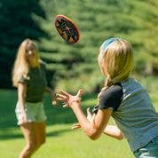 Two people toss the Indoor MayaFlya (Pocket Disc) on grass with trees in the background.