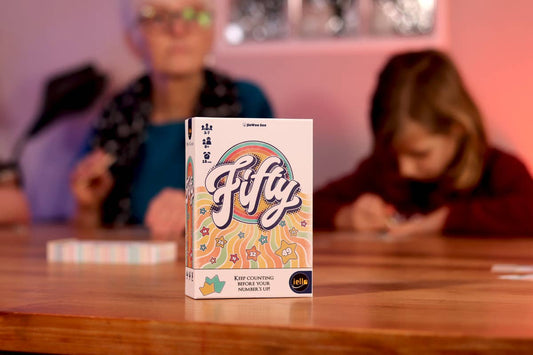 Fifty strategy board game on a table with two blurred players in the background.