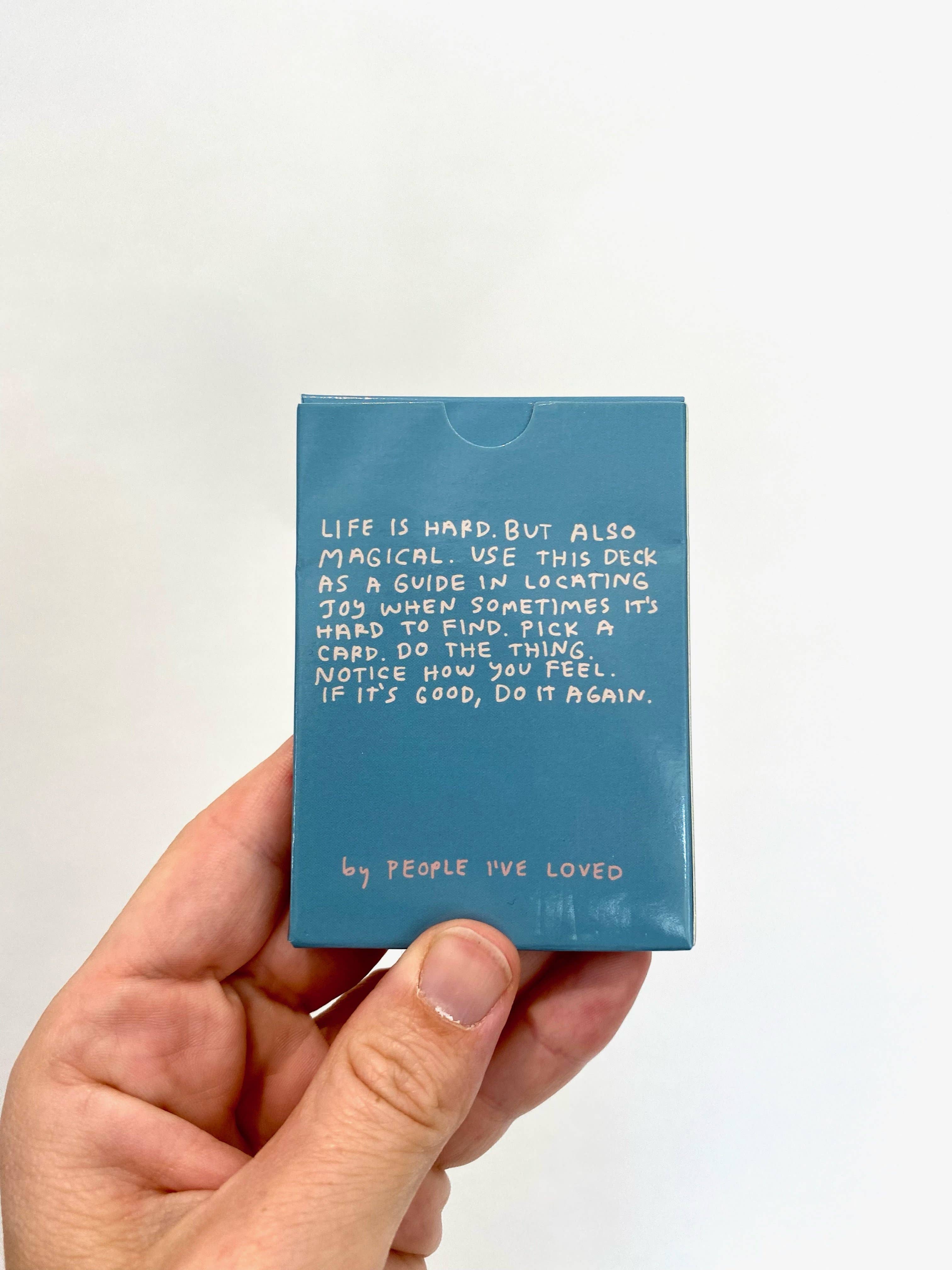 Blue Excuses To Celebrate Deck box with a white handwritten message, held in a hand.