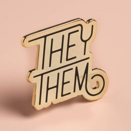 Gold pronoun pin with black text reading THEY/THEM.