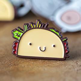 Taco Enamel Pin TCGCP showing a cartoon taco with smiling face, lettuce, and tomato.