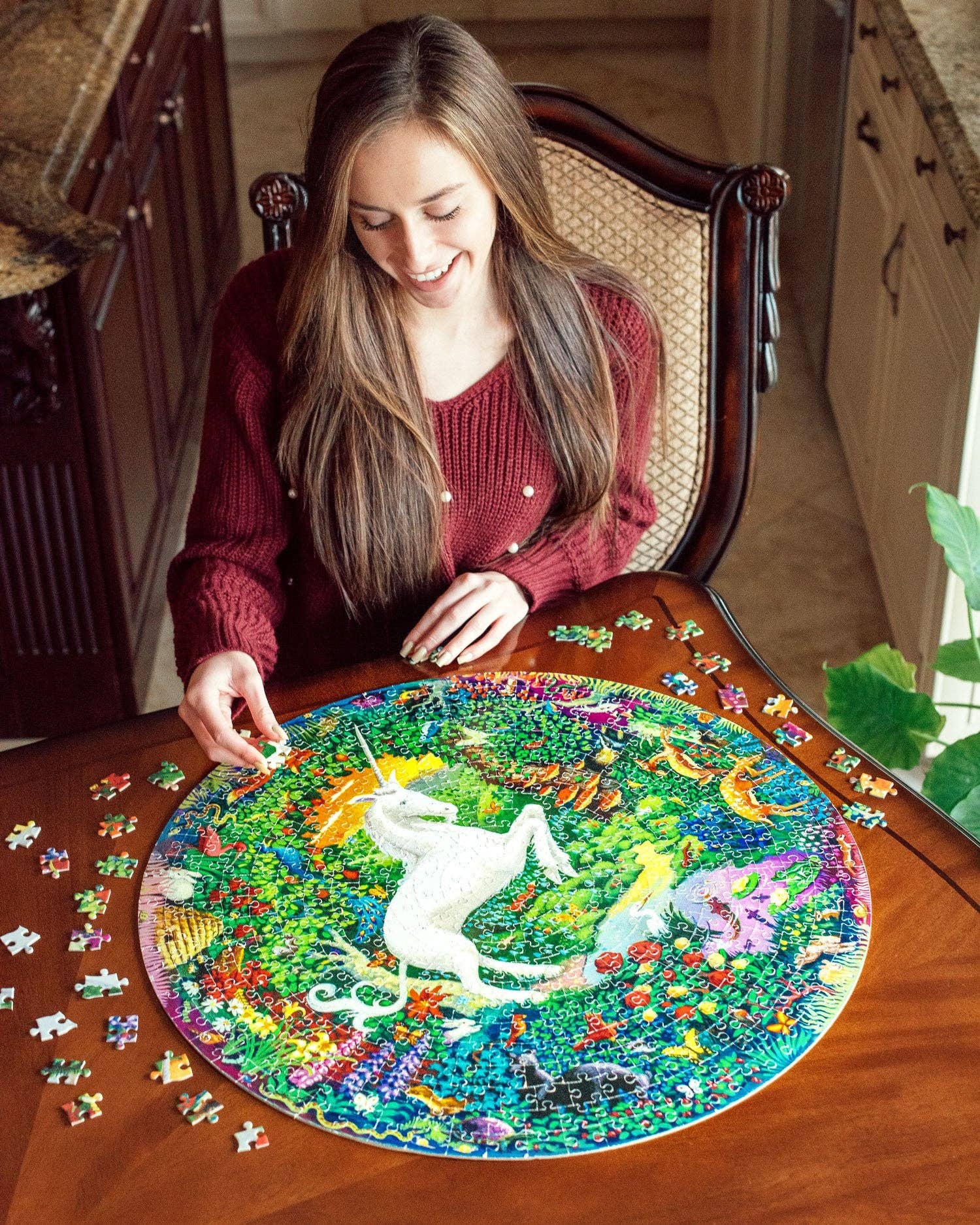 Unicorn Garden 500 Piece Round Puzzle being assembled on a wooden table by a woman in a red sweater.