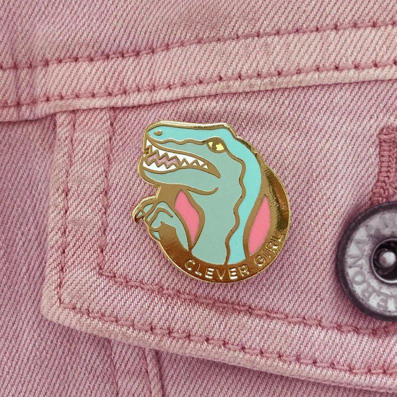 Clever Girl Velociraptor lapel pin on a pink denim jacket pocket.