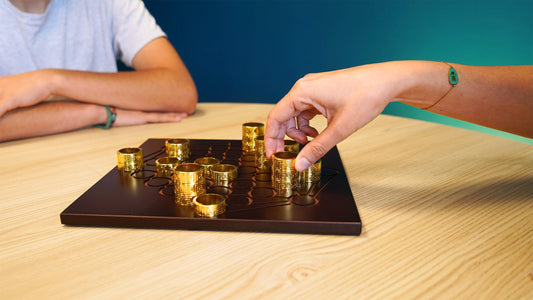 Two people playing Gygѐs board game with stacks of gold coins and mystical rings on a wooden table.