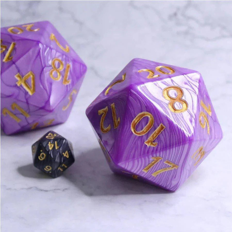 Two 55mm Titan D20 Purple Pearl dice with gold numbers and one small black die on a marble surface.