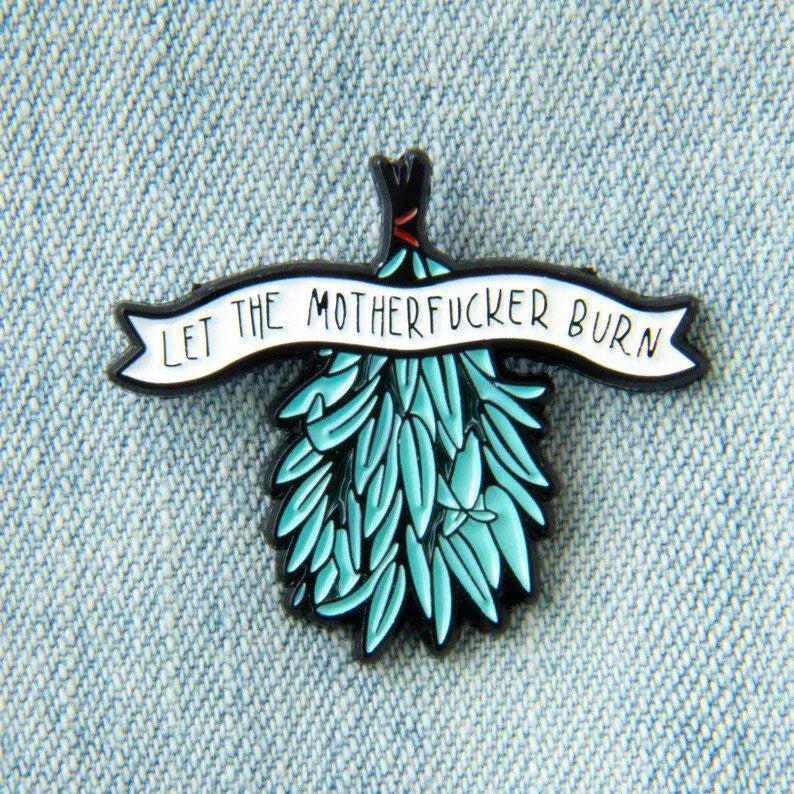 Sage smudging enamel pin featuring a blue pine tree and Let the Motherfucker Burn banner on light denim.