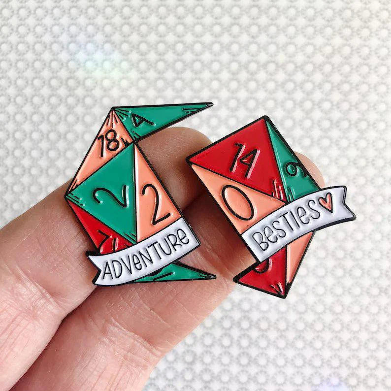 Adventure Besties D&D/RPG friendship enamel pins, two colorful dice-shaped pins held between fingers.
