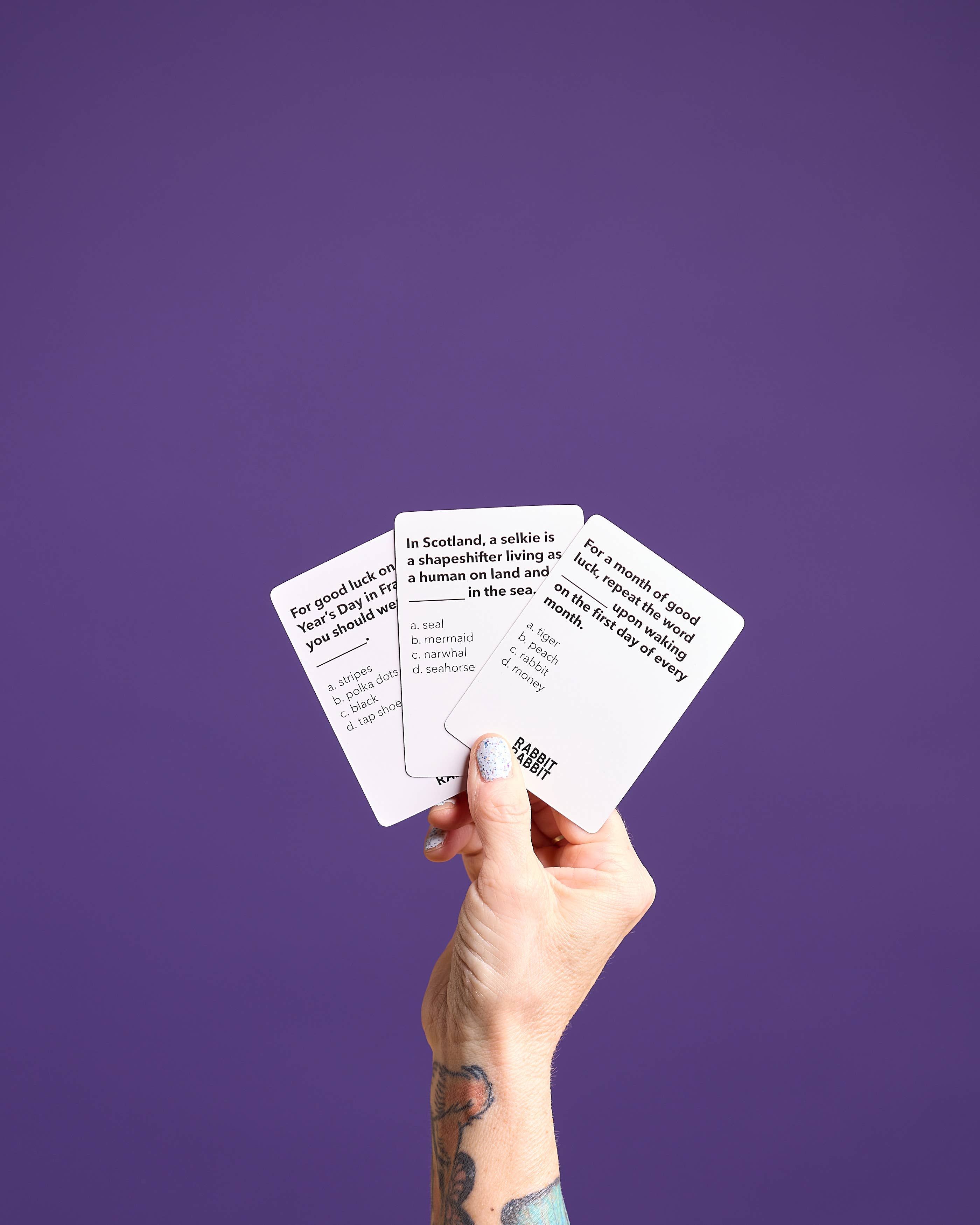 Three Rabbit Rabbit: A Game of Superstitions cards held by a tattooed hand.