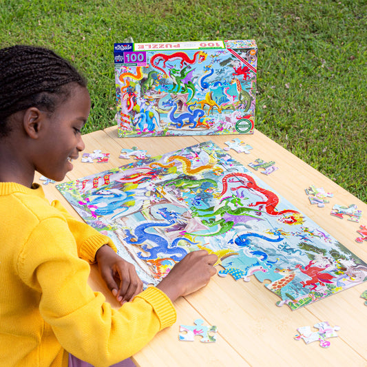 Love of Dragons 100 Piece Puzzle with colorful dragons being assembled on a wooden table outdoors.