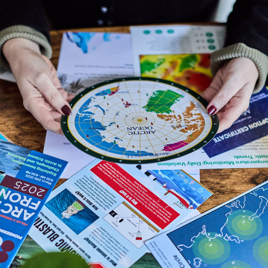 Escape Room in An Envelope - The Disappearance map held above climate puzzle pamphlets on a table.