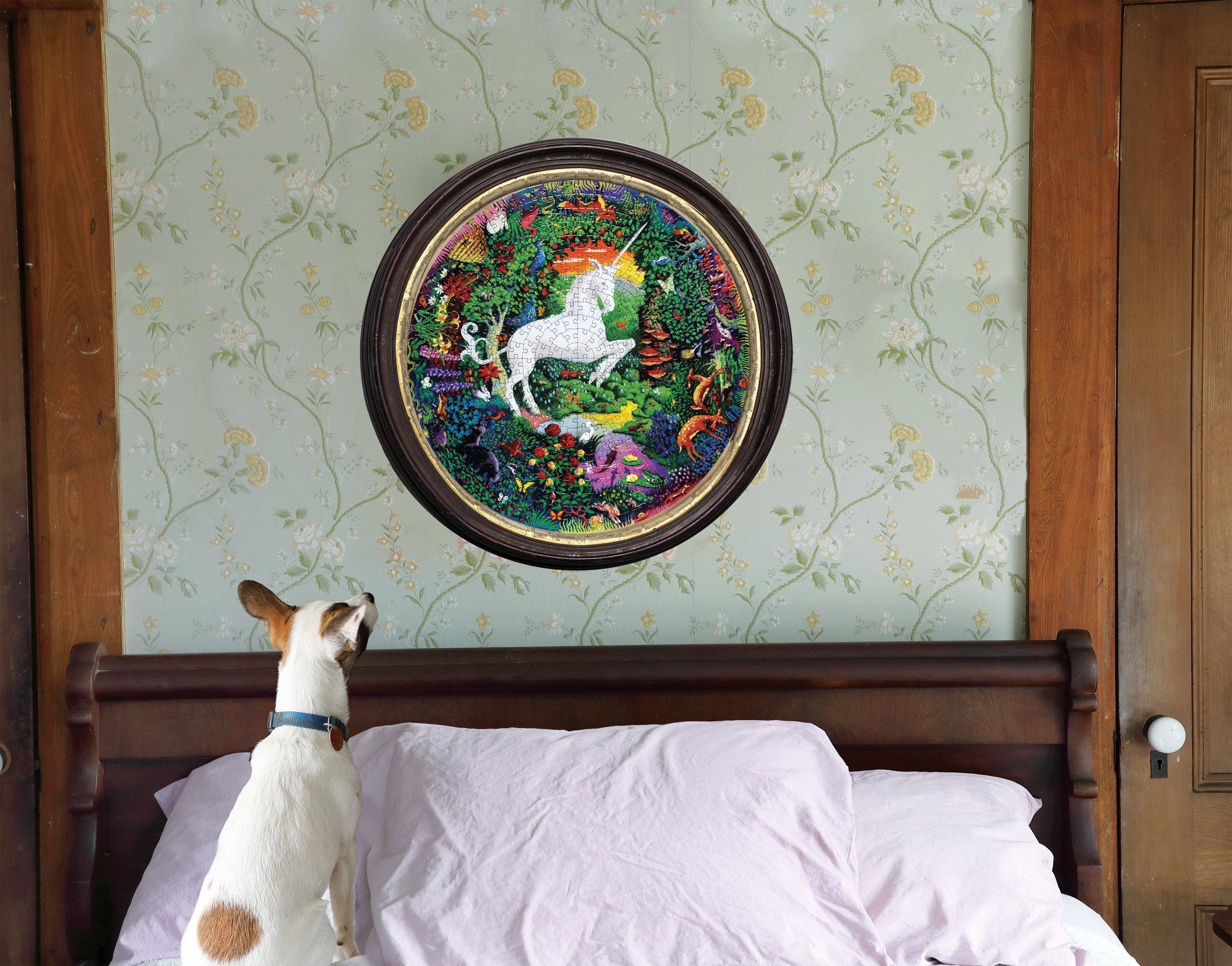 Unicorn Garden 500 Piece Round Puzzle displayed above a bed, with a dog looking up at it.