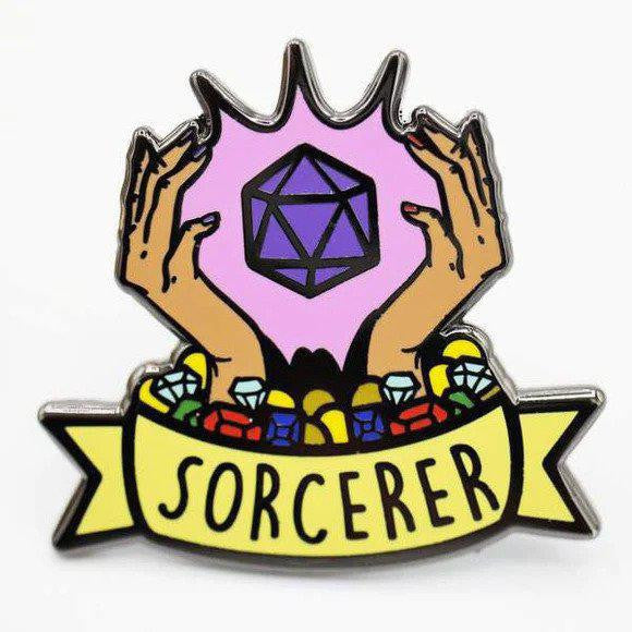 Enamel pin showing two hands conjuring a purple shape above gems, with a yellow Sorcerer Banner Class Pin below.