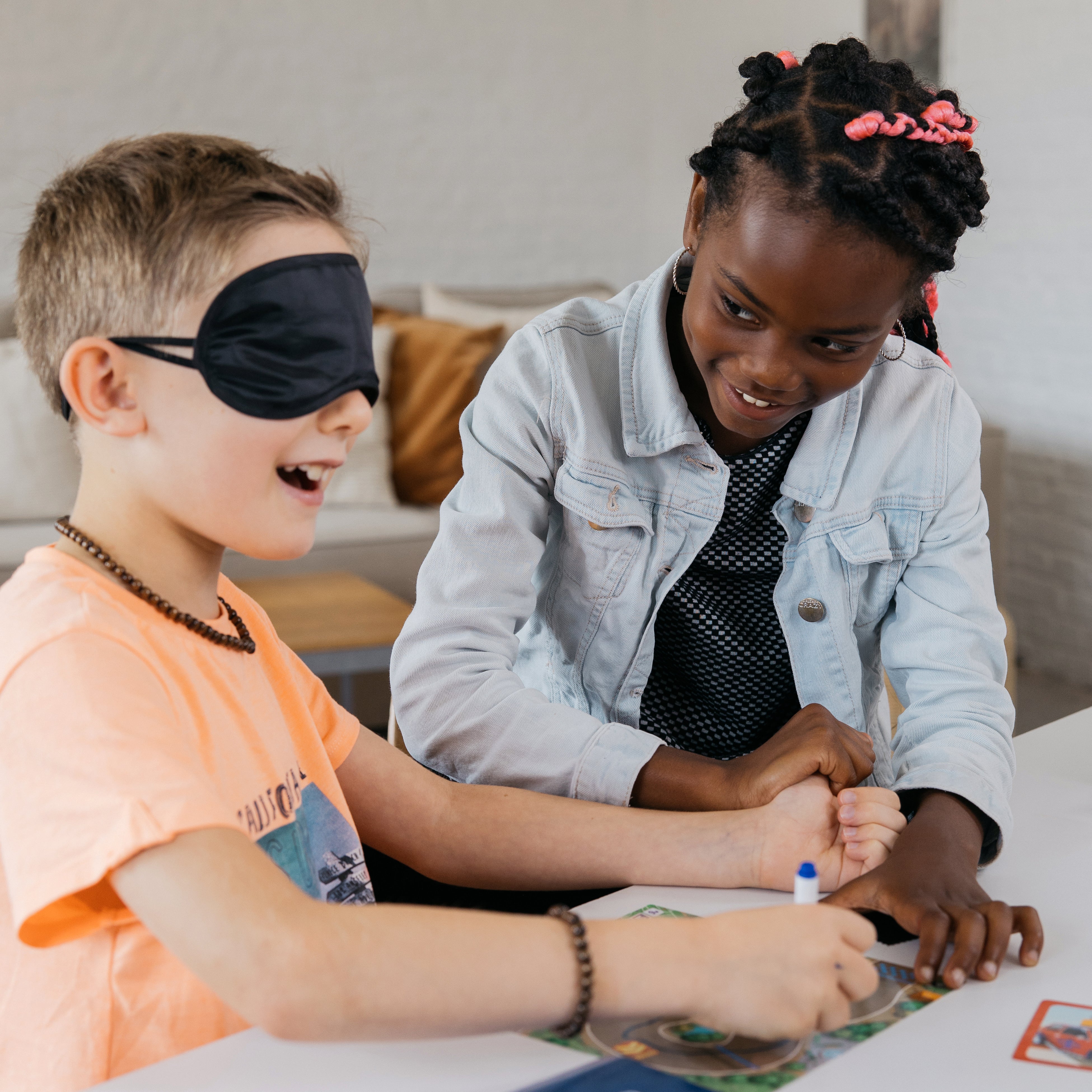 Children play Turbo Kidz party game; a blindfolded boy draws while a girl guides his hand.