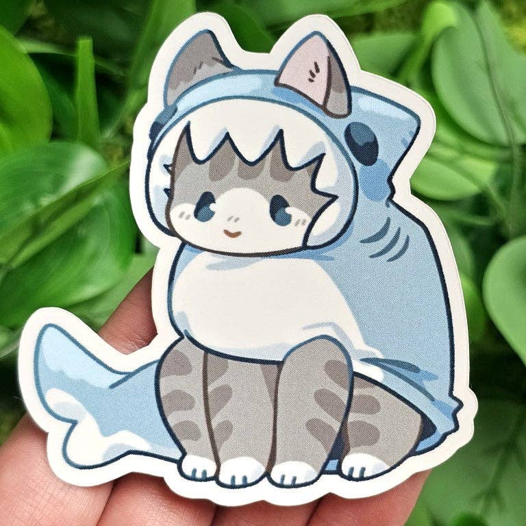 Cats in Sea Creature Costumes Stickers – cartoon cat in shark costume, green leaves in background.