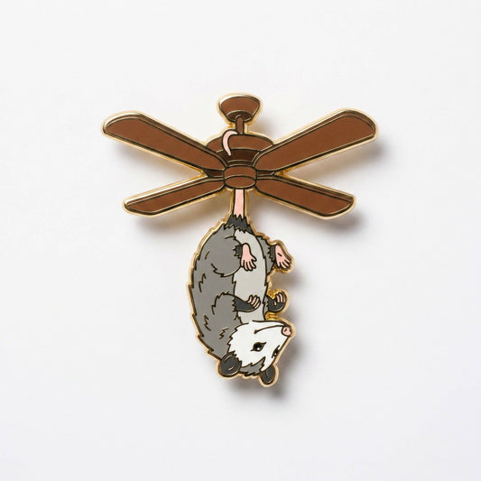 Possum Fan hard enamel pin, gold-plated, featuring a possum hanging from a brown ceiling fan.