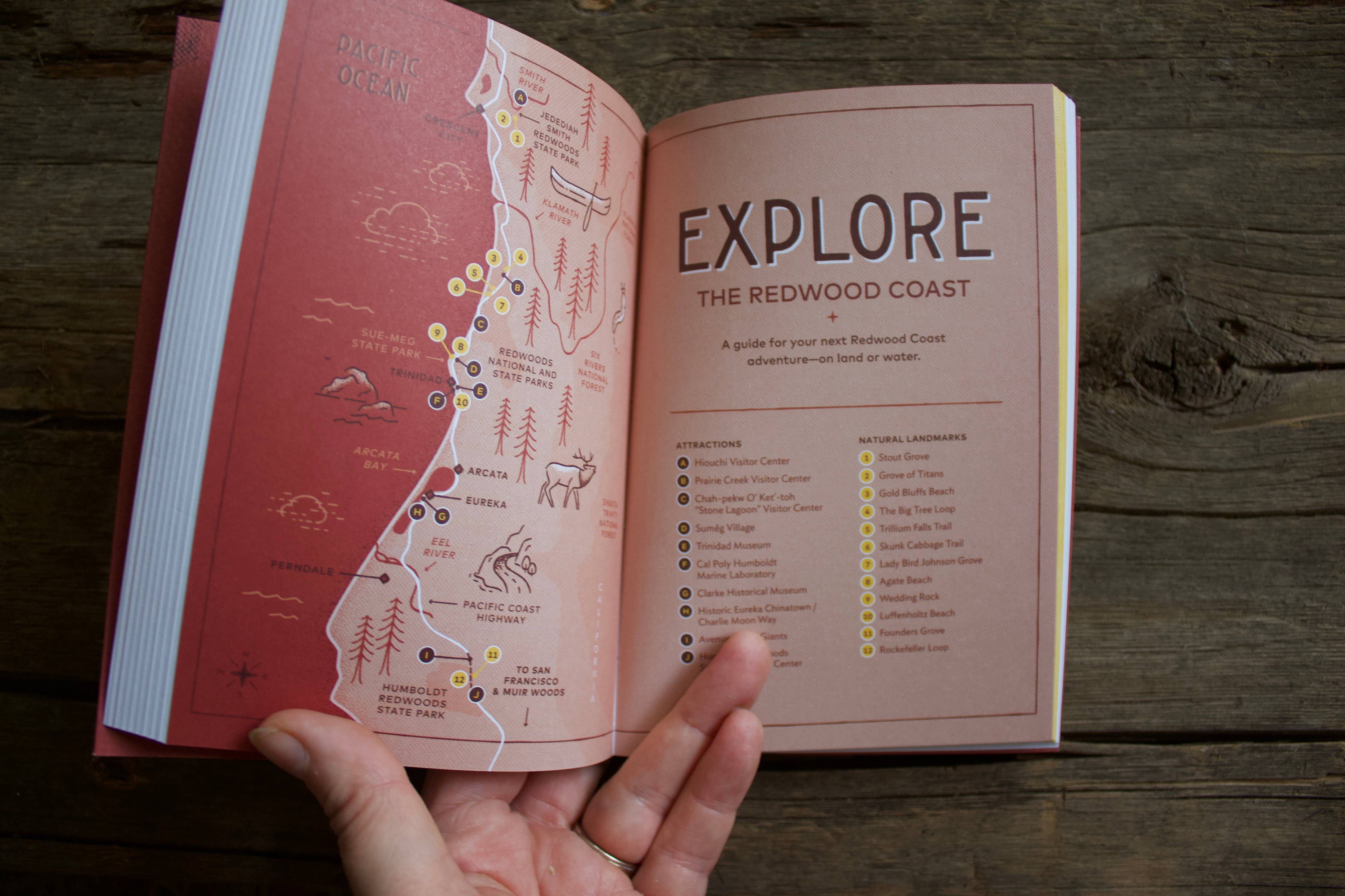 Campfire Stories: The Redwood Coast sustainable travel guide with local map printed on wood, held open by a hand.